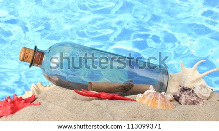 Glass bottle with note inside on sand, on blue sea background