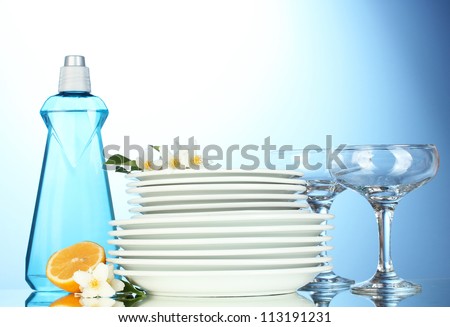 empty clean plates and glasses with dishwashing liquid, sponges and lemon on blue background