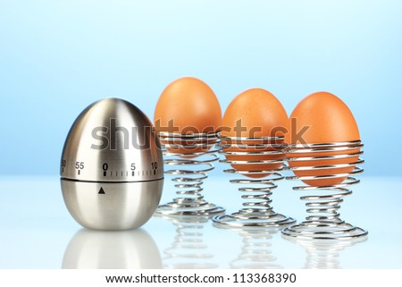 egg timer and egg in metal stand on blue background