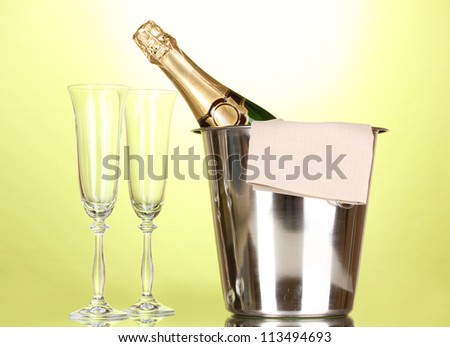 Champagne bottle in bucket with ice and glasses on green background