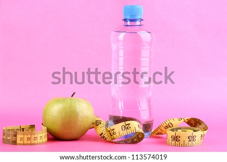 Bottle of water, apple and measuring tape on pink background