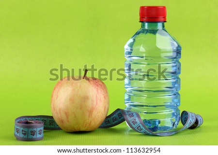 Bottle of water, apple and measuring tape on green background