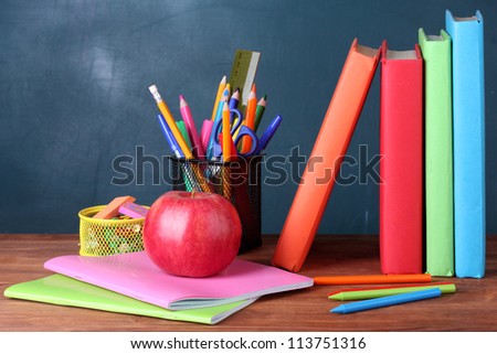 Composition of books, stationery and an apple on the teacher\'s desk in the background of the blackboard
