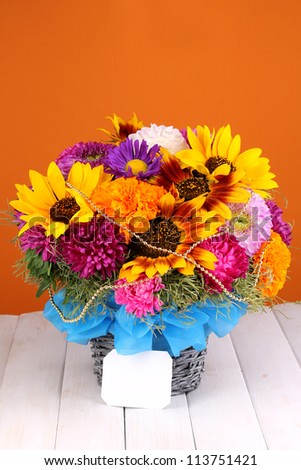 Beautiful bouquet of bright flowers with paper note on wooden table on orange background