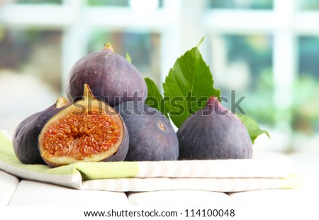 Ripe sweet figs with leaves, on wooden table, on window background
