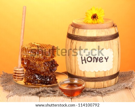 Barrel of honey and honeycomb on wooden table on orange background