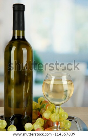 White wine in glass with bottle on salver on room background