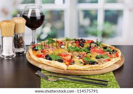Delicious pizza with glass of red wine and spices on wooden table on window background
