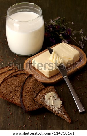 Butter on wooden holder surrounded by bread and milk on wooden table close-up