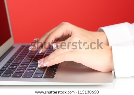 Hands typing on laptop keyboard close up on  red background