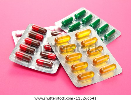 Capsules and pills packed in blisters, on pink background