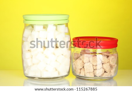 Jars with brown cane sugar lump and white lump sugar on colorful background