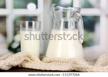 Pitcher and glass of milk on crewnecks knitwear on wooden table on window background