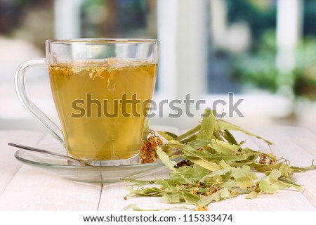 Glass cup of tea with linden on wooden table on window background