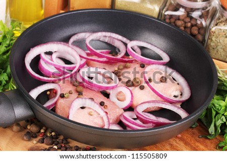 A pieces of pork with onions fried in pan with herbs, spices and cooking oil on board close-up