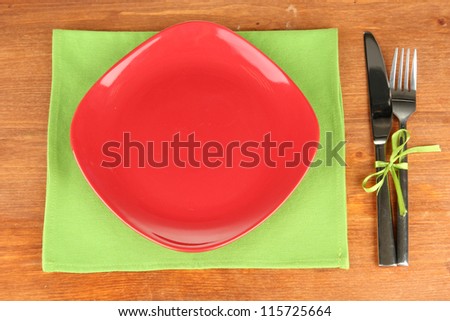 Empty square red plate with fork and knife on wooden table, close-up
