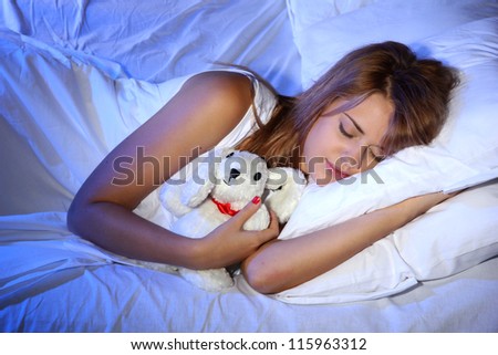 young beautiful woman with toy rabbit sleeping on bed in bedroom