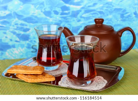 glass of Turkish tea and kettle on color background
