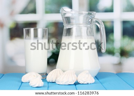 Pitcher and glass of milk with meringues on wooden table on window background