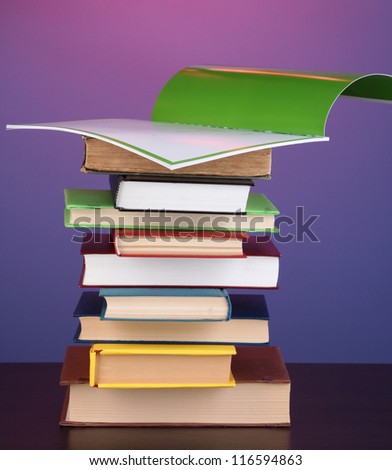 Stack of interesting books and magazines on wooden table on purple background