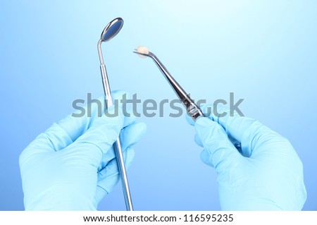 Hands in blue gloves holding dental tools on blue background