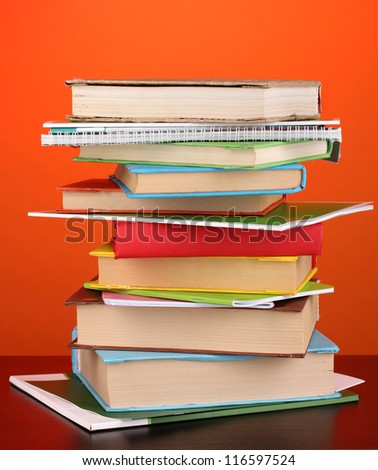 Stack of interesting books and magazines on wooden table on red background