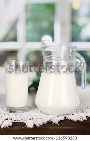 Pitcher and glass of milk on wooden table on window background