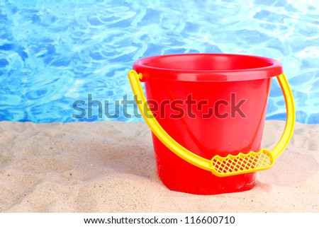 Children's bucket on sand on water background