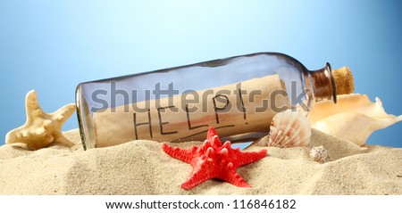 Glass bottle with note inside on sand, on blue background