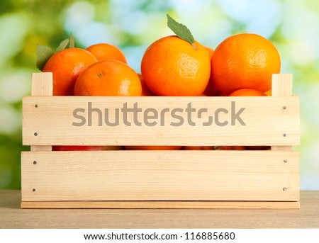 Ripe tasty tangerines with leaves in wooden box on table on green background