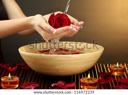 woman hands with wooden bowl of water with petals, on brown background