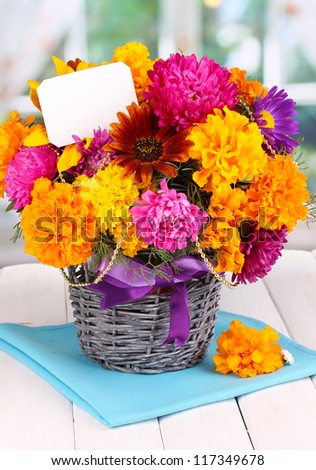 Beautiful bouquet of bright flowers with paper note on wooden table on window background