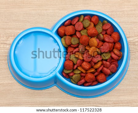 dry dog food and water in blue bowl on wooden background