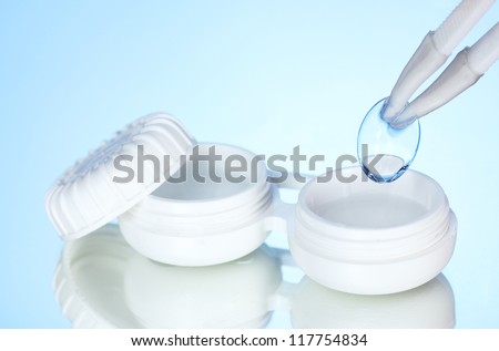 contact lenses in containers and tweezers on blue background
