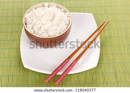 Bowl of rice and chopsticks on plate on bamboo mat