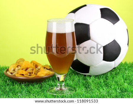 Glass of beer with soccer ball on grass on green background
