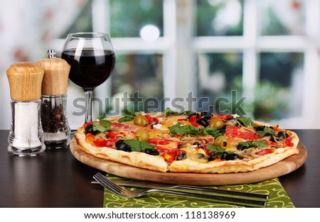 Delicious pizza with glass of red wine and spices on wooden table on window background
