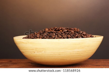 Coffee beans in bamboo bowl on table on brown background