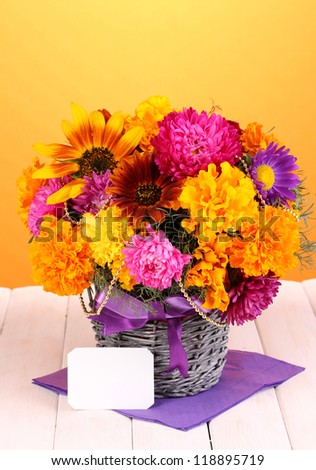 Beautiful bouquet of bright flowers with paper note on wooden table on yellow background