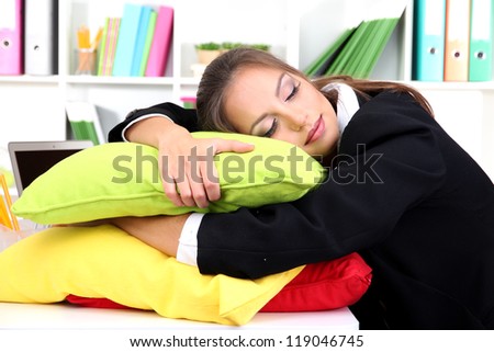 Tired business woman with pillows sitting at the table and sleeps