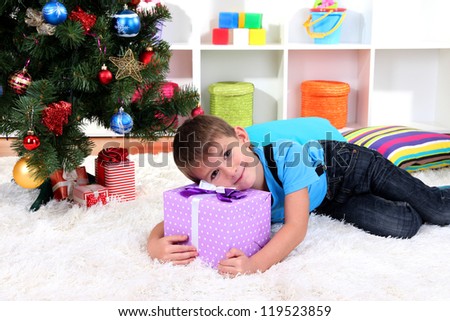 Little boy lying on gift in his hands under Christmas Tree waiting for Santa Claus to come
