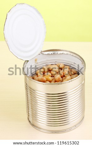 Open tin can of bean on wooden table on green background