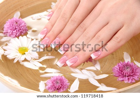 Woman hands with french manicure and flowers in bamboo bowl with water