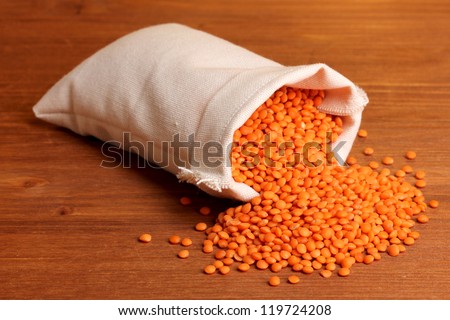 Cloth bag of lentil on wooden table on brown background