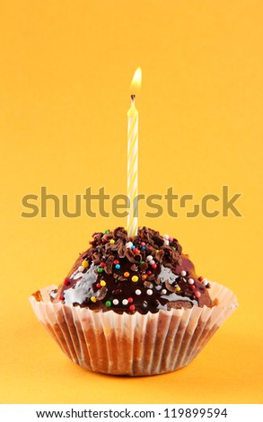 tasty birthday cupcake with candle, on orange background