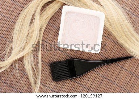 hair dye in bowl and brush for hair coloring on brown bamboo mat, close-up