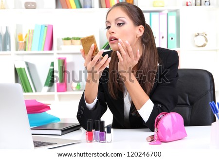 young business woman looking in the mirror and putting some makeup by office work