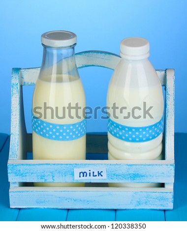 Milk in bottles in wooden box on blue wooden table on blue background