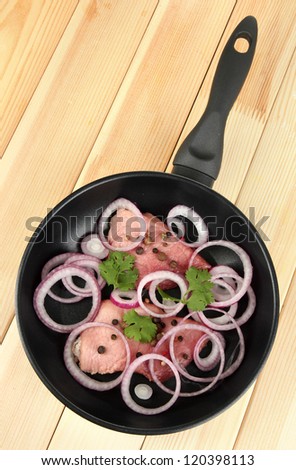 A pieces of pork with onions fried in pan on wooden table