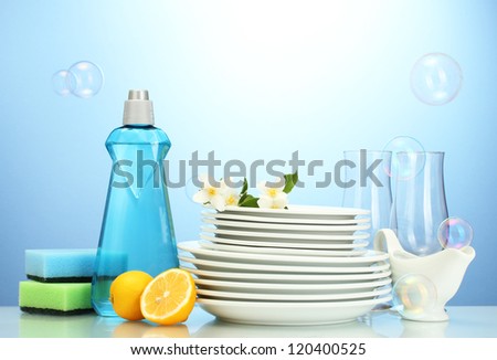 empty clean plates and glasses with dishwashing liquid, sponges and lemon on blue background